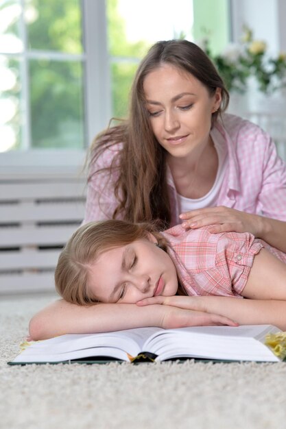 Mother waking up her little daughter who sleeping on opened book