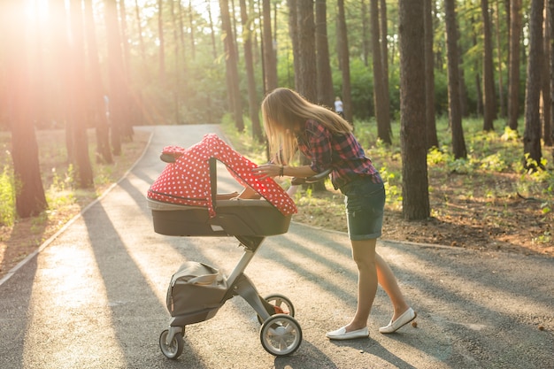 Foto madre che cammina mentre spinge un passeggino nel parco.