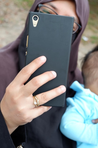 Photo mother wearing hijab taking selfie with daughter while sitting outdoors