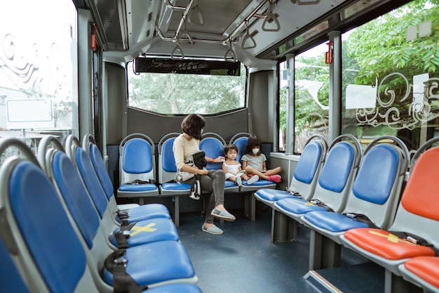 A mother wearing a mask and her two daughters sit in the back seat of the bus on the way