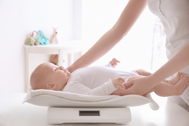 Mother weighting baby on scales in room