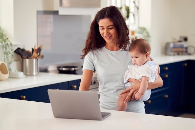 부엌에서 노트북으로 집에서 일하는 아기 아들과 어머니