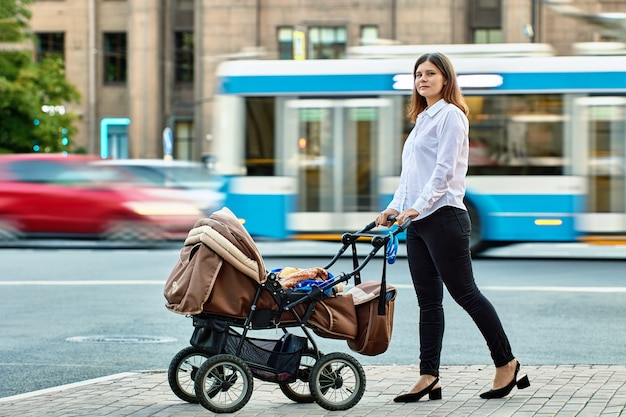 乳母車に子供を持つ母親が交通の近くを歩く