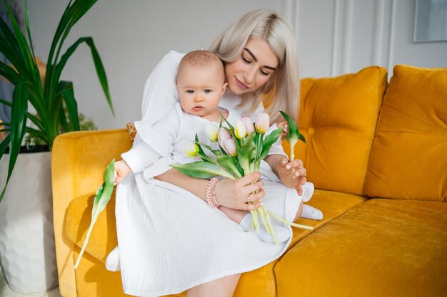 Фото Мать с ребенком в белой одежде на желтом диване букет цветов тюльпанов весна