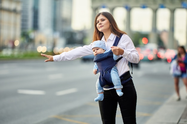 Madre con bambino in fascia sta fermando un taxi per strada