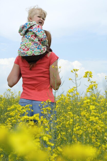 Mother with child on a yellow field in bloom with blue sky and white clouds