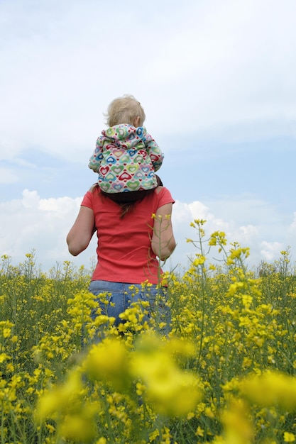 Мать с ребенком на желтом поле в цвету с голубым небом и белыми облаками