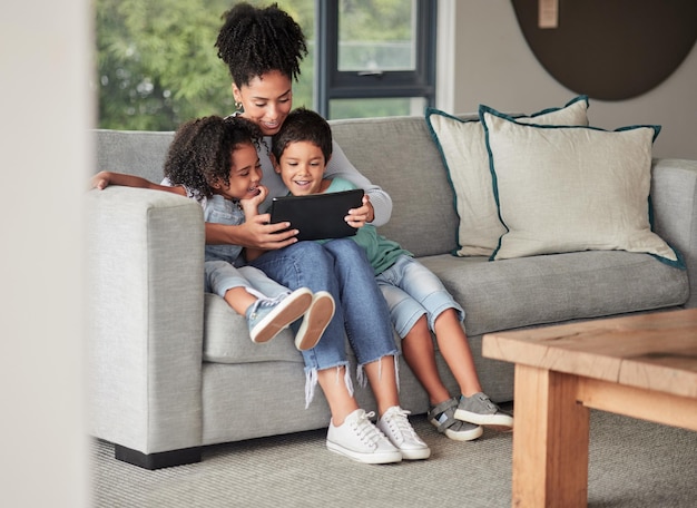 A mother with children on couch with tablet to watch educational shows and streaming music Foster or adoption parent with kids in living room watch cartoons playing online games and homeschooling