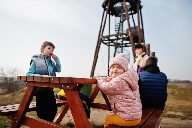 Mother with children sit at wooden table against observation tower