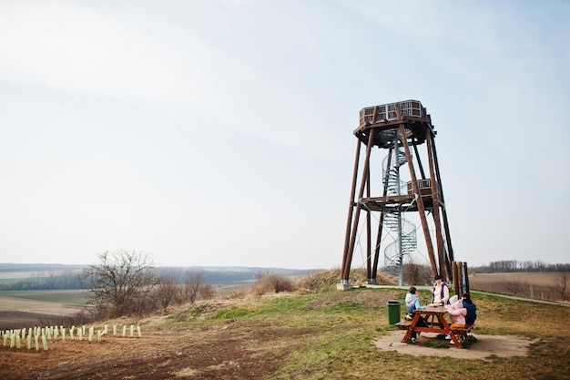 Mother with children sit at wooden table against observation tower