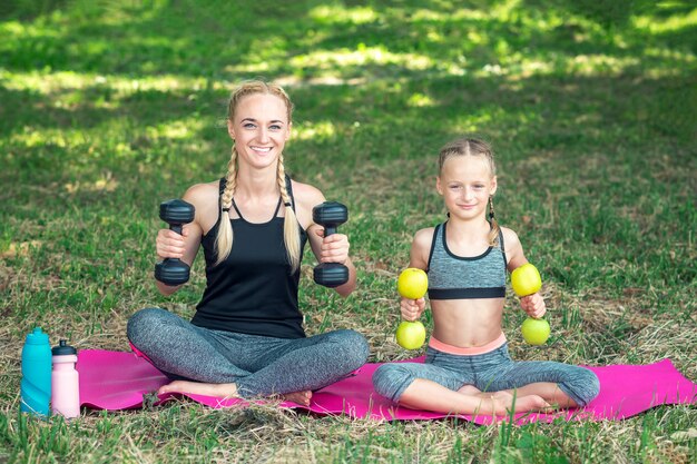 Mother with daughter are training with dumbbells on the roll mat at the park