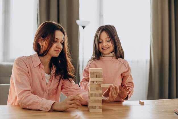 Mother with daughter building wooden jenga blocks into tower