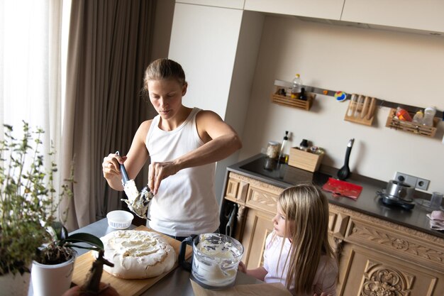 Photo mother with daughter child preparing sweet dessert cream cake in home kitchen