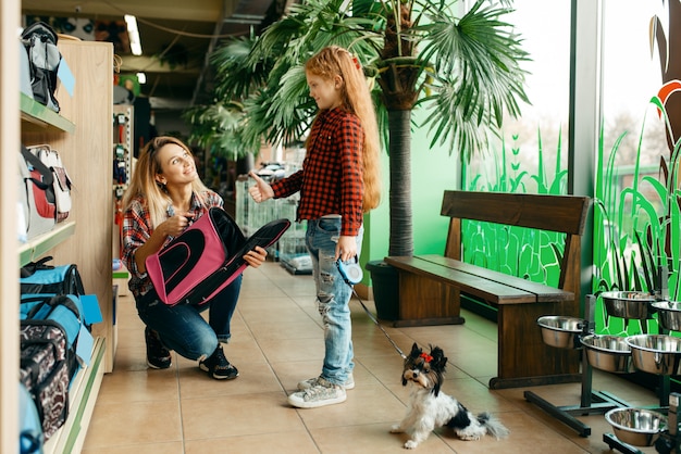 Mother with daughter choosing bag for little puppy in pet store.