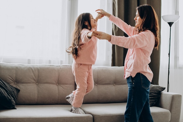 Mother with daughter dancing at home on sofa