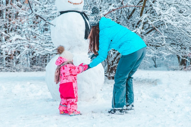 Mother with daughter playing outside in winter time. making snowman concept