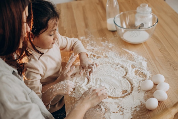 Mother with daughter playing with flour and making heart on it at kitchen