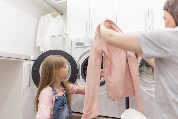 mother with daughter removing clothes from washing machine at home