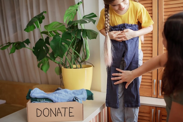 Mother with daughter sort out the wardrobe and collect clothes for donate box at home, second hand