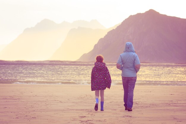 Mother with daughter walking by sandy beach at sunset time