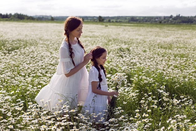 흰 드레스와 모자에 딸과 어머니는 여름에 데이지 필드에 서