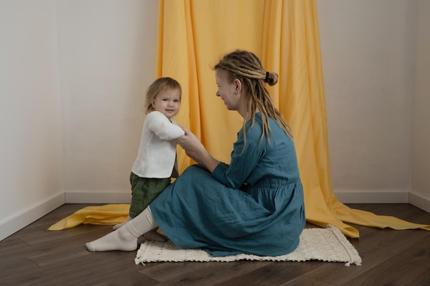 A mother with dreadlocks and a child sit on the carpet and spend time together Mom's day