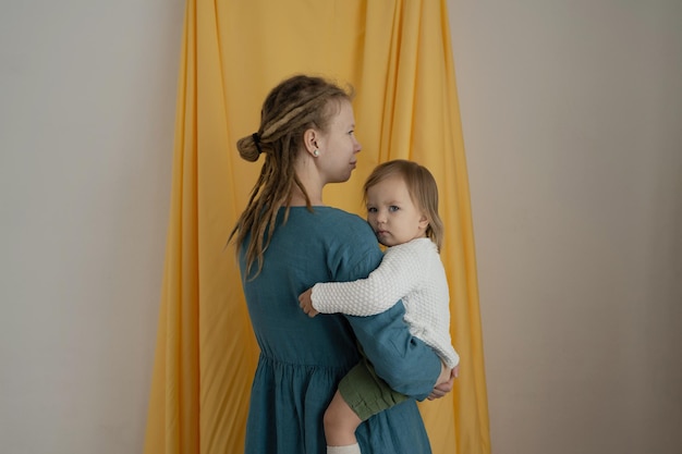 A mother with dreadlocks with a baby in her arms on a fabric yellow background Closeup