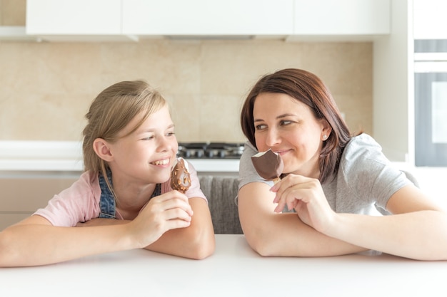 Madre con la figlia di 12 anni seduta in cucina a mangiare il gelato, buoni rapporti di genitore e figlio, momenti felici insieme