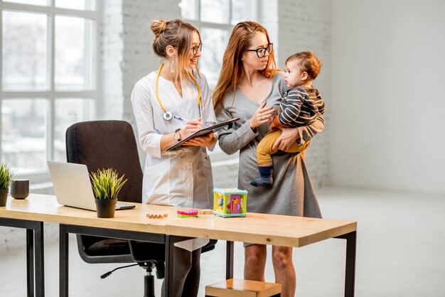 Mother with her baby boy during the consultation with young woman pediatrician standing in the white office