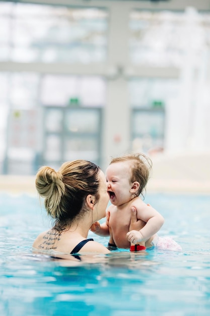 Mother with her baby daughter swim in the pool in waterpark first swimming