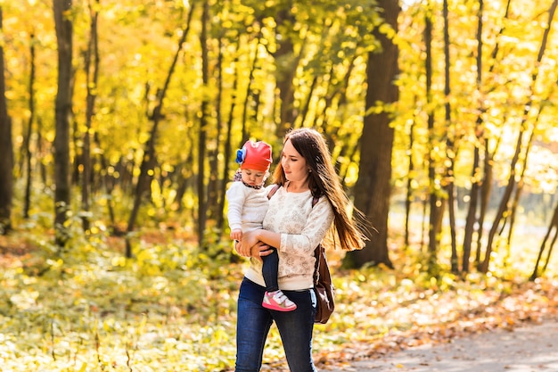 赤ちゃんを持つ母親。秋の公園でママと娘。