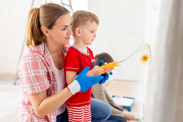 Mother with her children painting the wall with paint using roller and brush