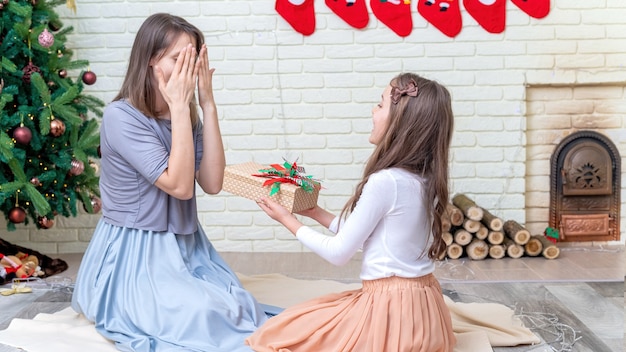 Mother with her daughter are giving gifts on the floor near the christmas tree at home. Happy family idea