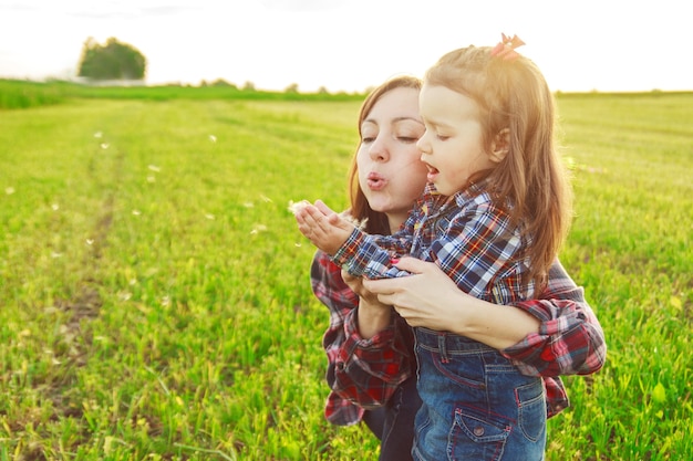 Mother with her daughter in the field blowing a dendelion