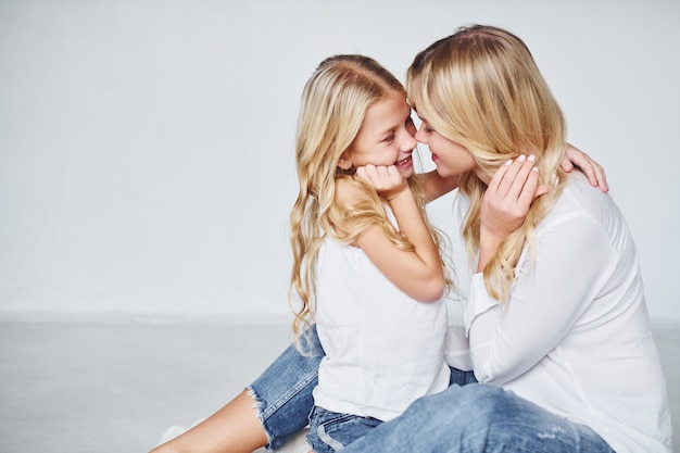 Photo mother with her daughter together is on the ground in the studio with white background.