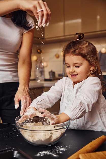 Mother with her little daughter preparing food on kitchen and have fun.