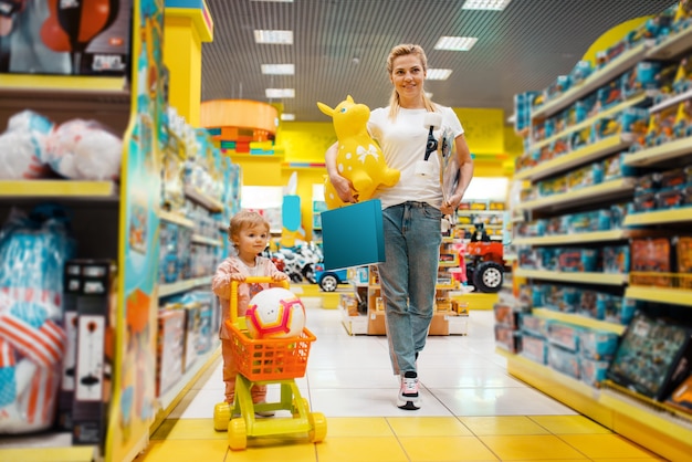 Mother with her little girl buying a lot of toys in kids store.