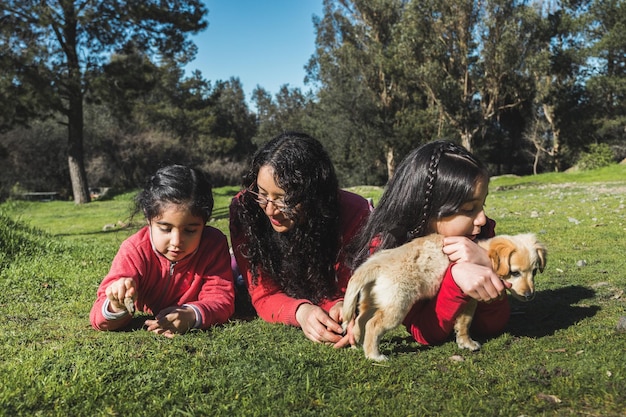 Mother with her two daughters, playing with a golden retriever puppy in the park. Female family