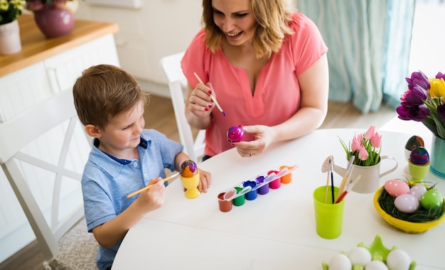 Mother with kid making easter decoration and painting eggs