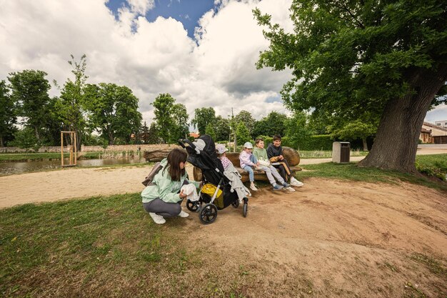 座っていると、公園の屋外の木製のベンチで休んでいる子供を持つ母