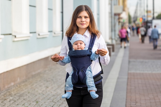 Mother with little child in sling walks on street