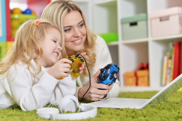 Mother with little daughter playing computer games with laptop