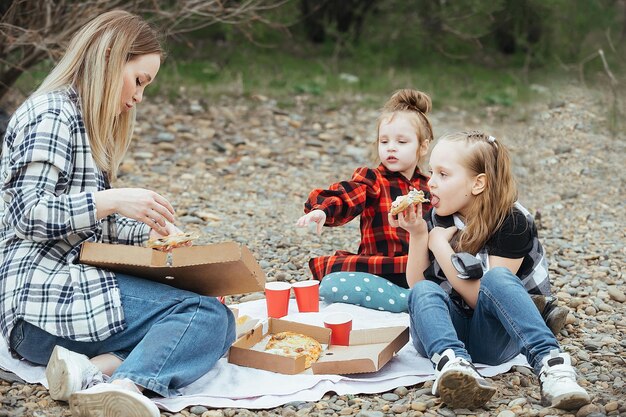 mother with little daughters on a picnic in nature by the river outside the city