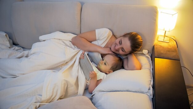 Mother with little son lying in bed and using tablet computer.