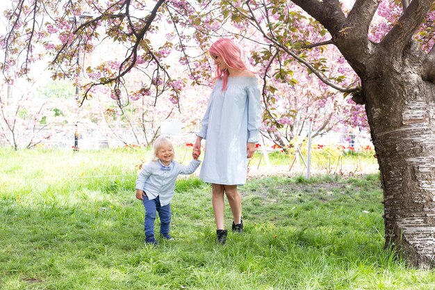 Mother with little son in the park walking near the sakura tree