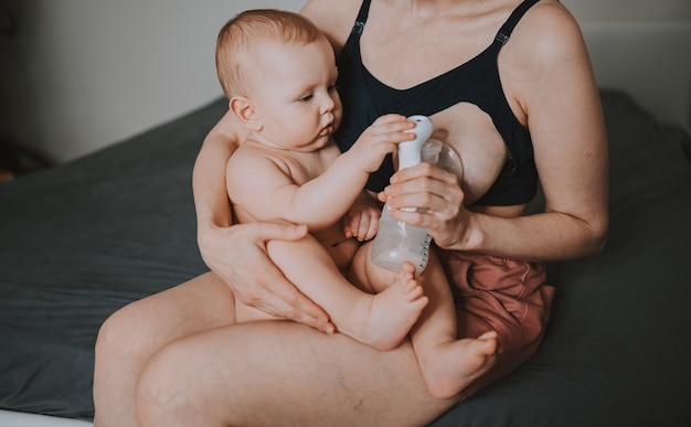 Mother with newborn baby boy holding him in her arms using breast pump hugging