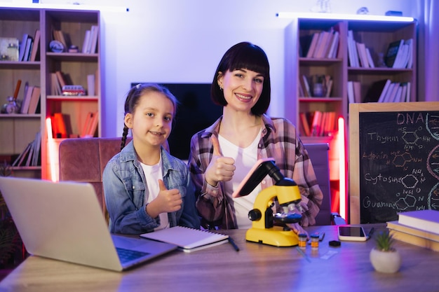 Mother with school daughter working with electronic microscope