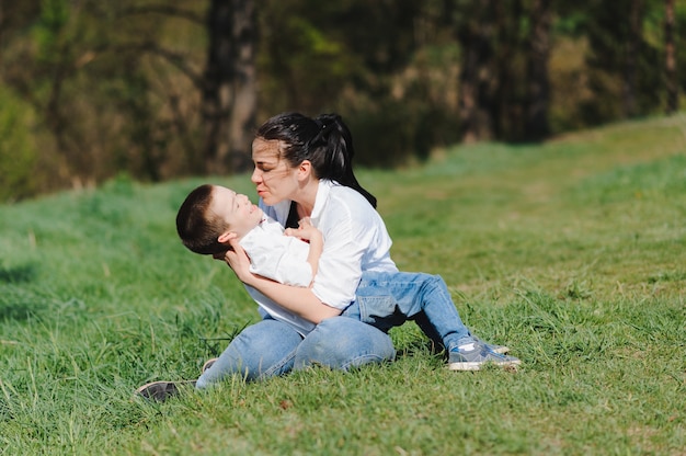 Мать с сыном ребенок играет вместе весело на траве в солнечный летний день