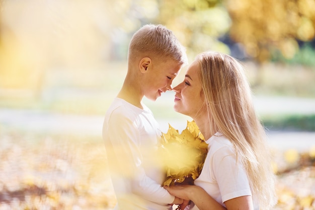 Mother with son have a rest in an beautiful autumn park at sunny day.