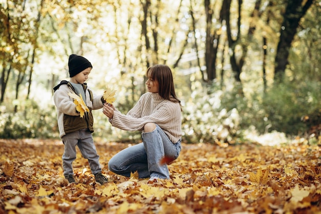 Madre con figlio che si diverte nel parco autunnale giocando con le foglie